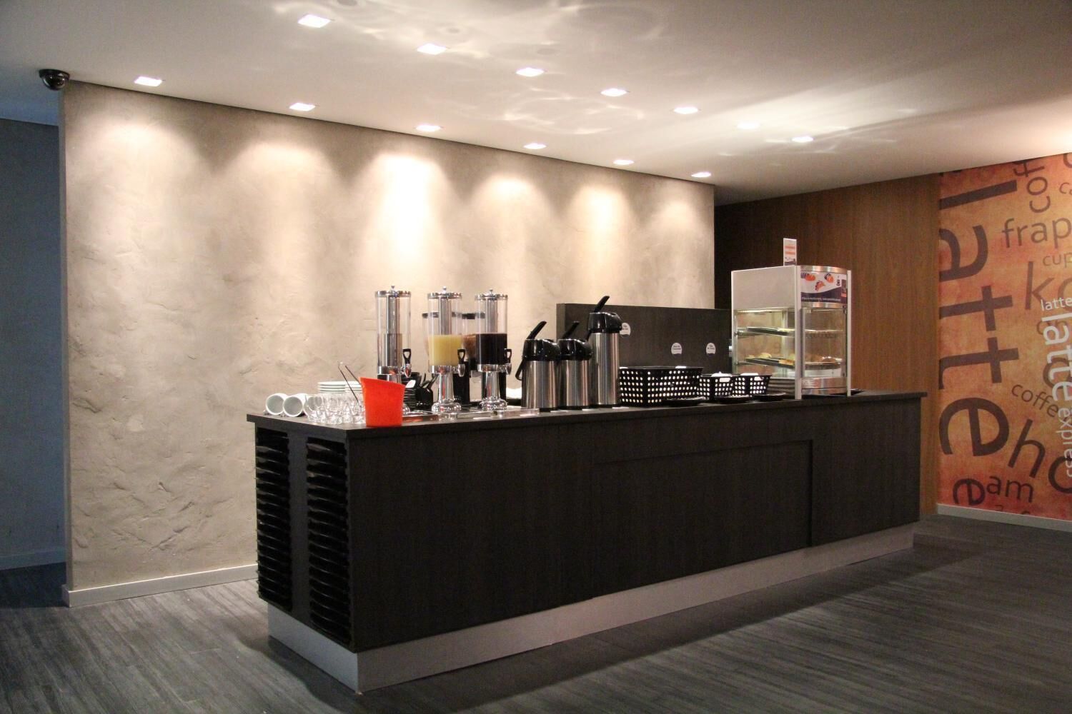Un área de recepción moderna con mostrador, máquinas de café y una pared con texto sobre café.