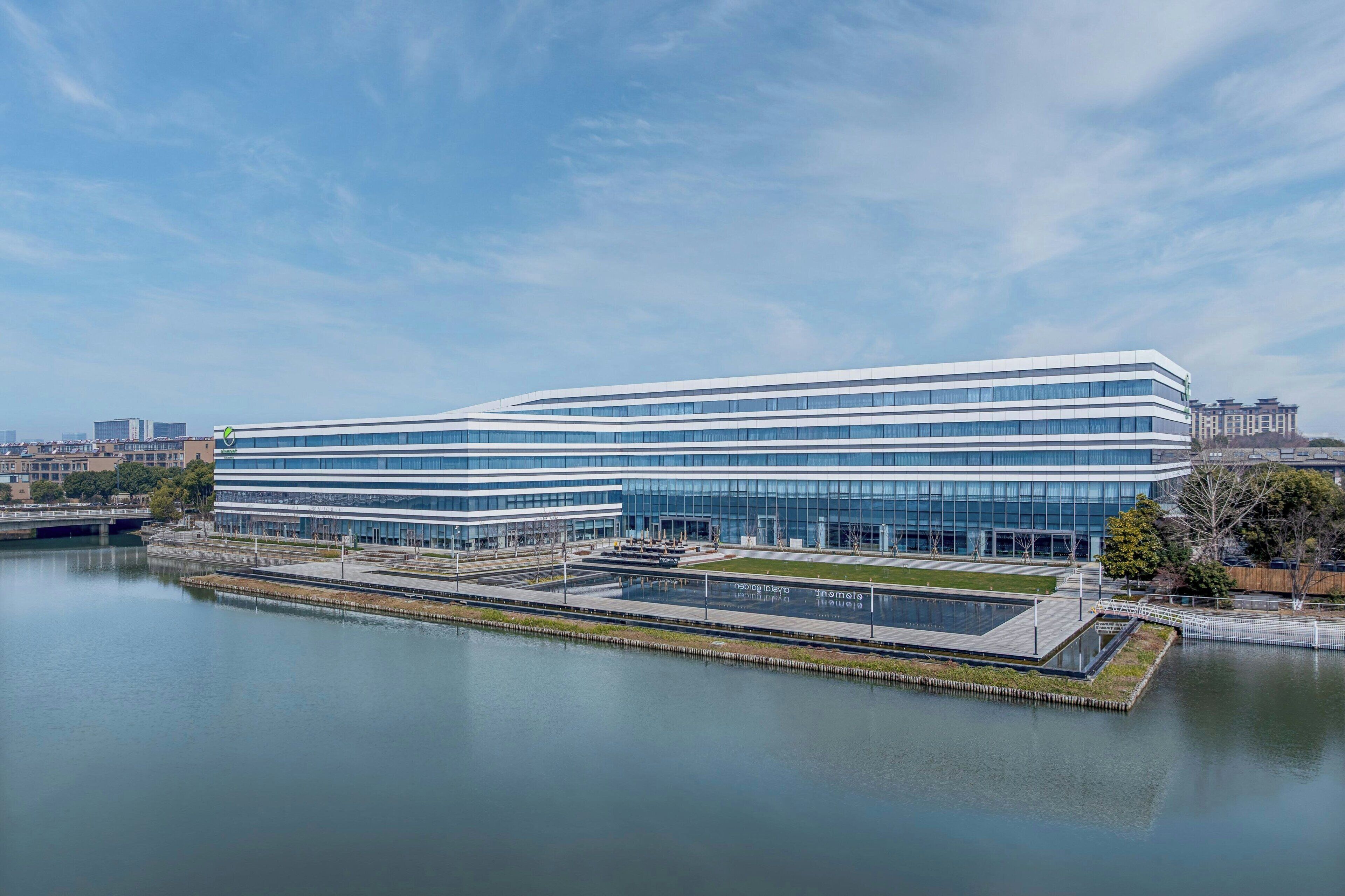 A modern building with a glass facade, a waterfront view, and a landscaped area with a small pool.