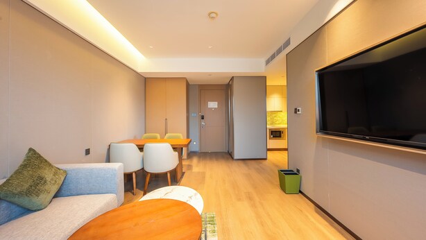 A modern hotel room with a sofa, a dining table, chairs, a TV, and a trash bin. - Element Suzhou Science and Technology Town (Suzhou)