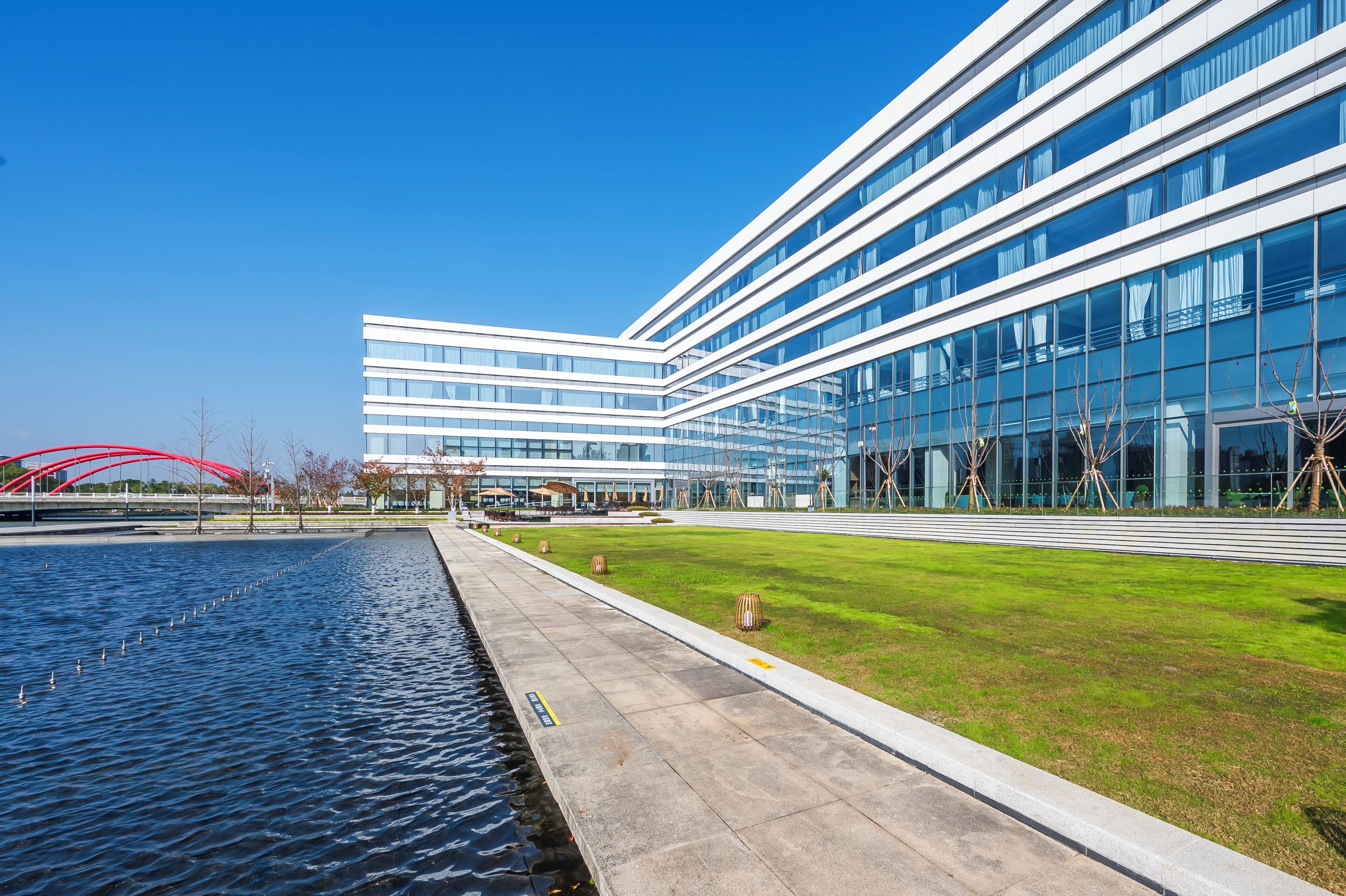 A modern building with a glass facade, a grassy area, and a water feature.