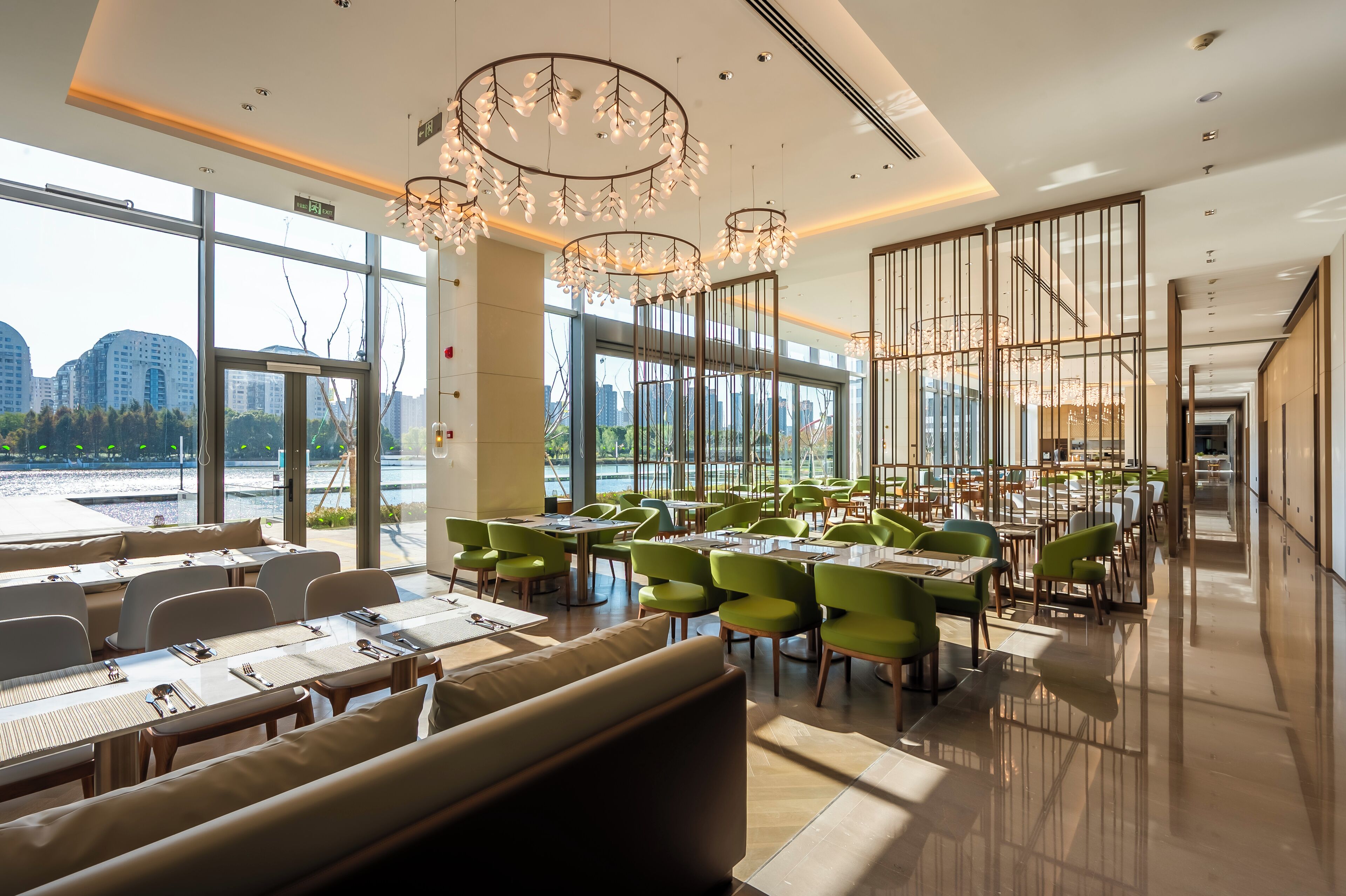 Un restaurant moderne avec de grandes fenêtres, des chaises vertes et un lustre.
