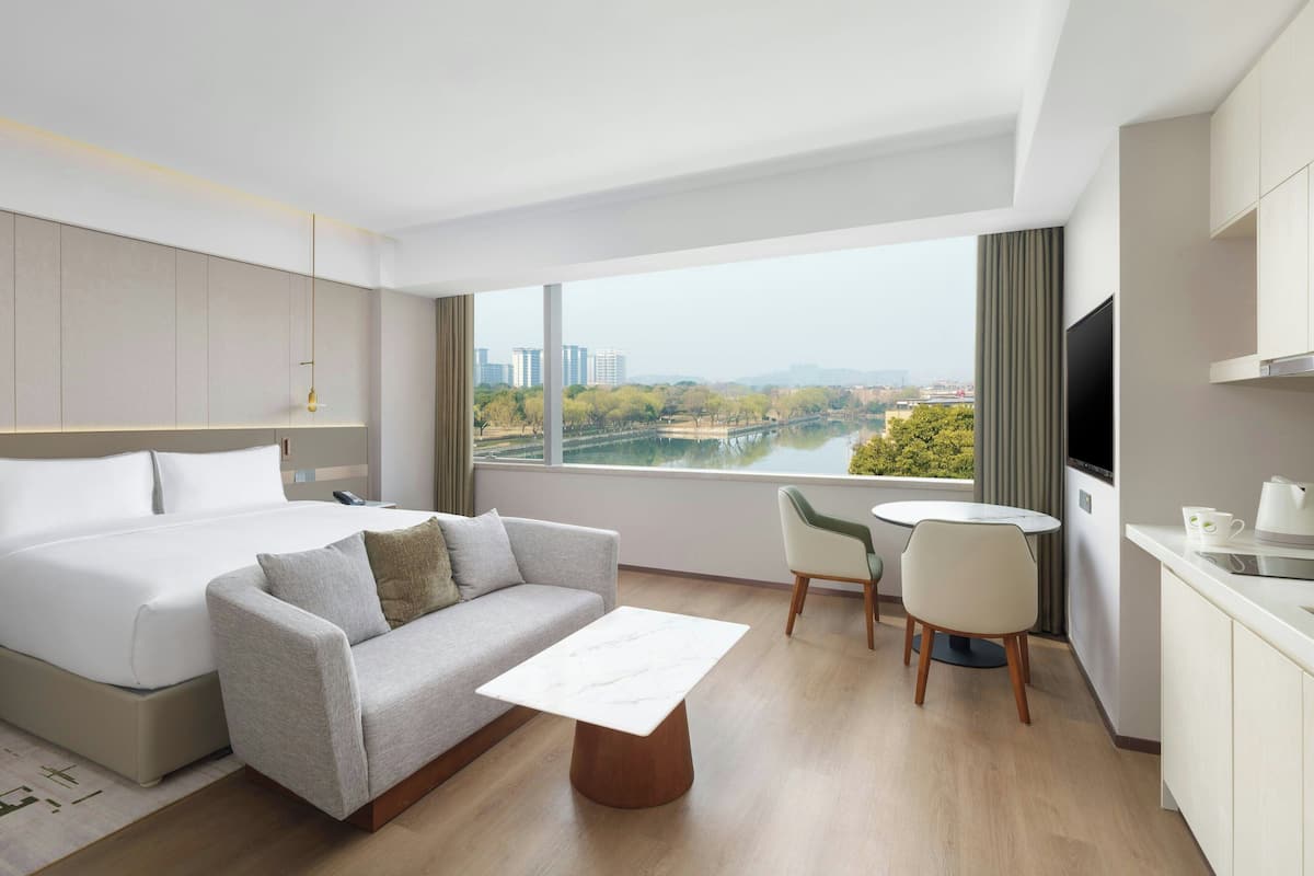 Habitación de hotel moderna con cama, sofá, mesa de centro, televisión y vista a un río y edificios.