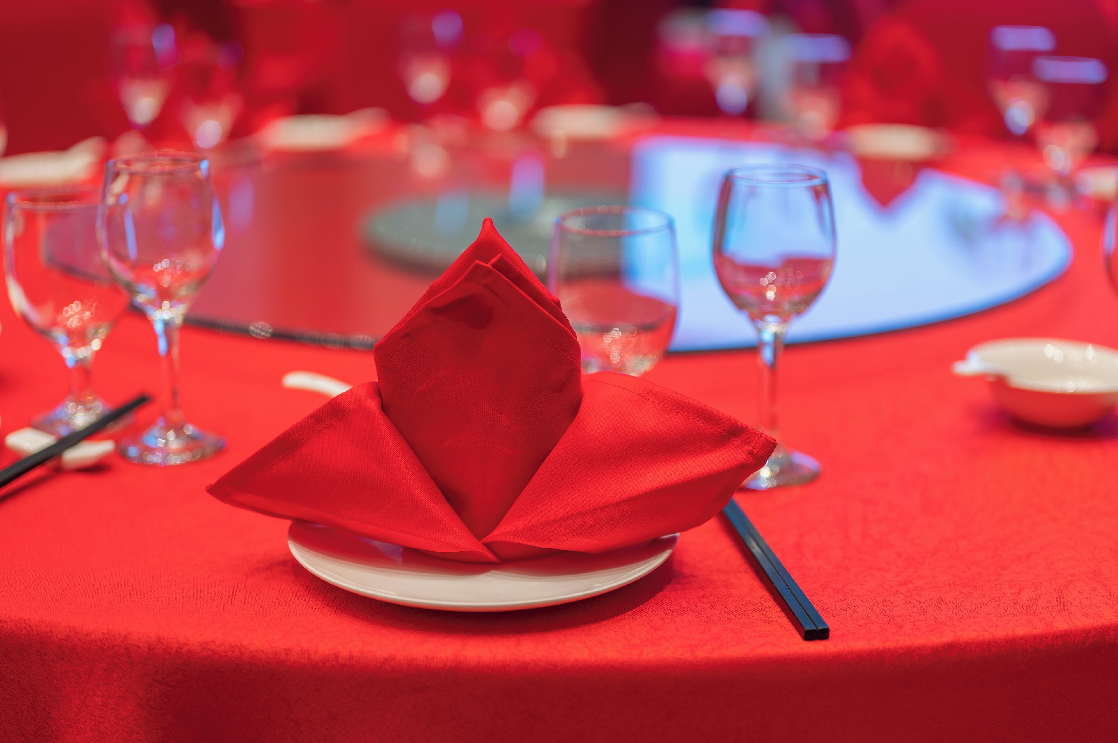 A table set with a red tablecloth, a folded napkin, and wine glasses.