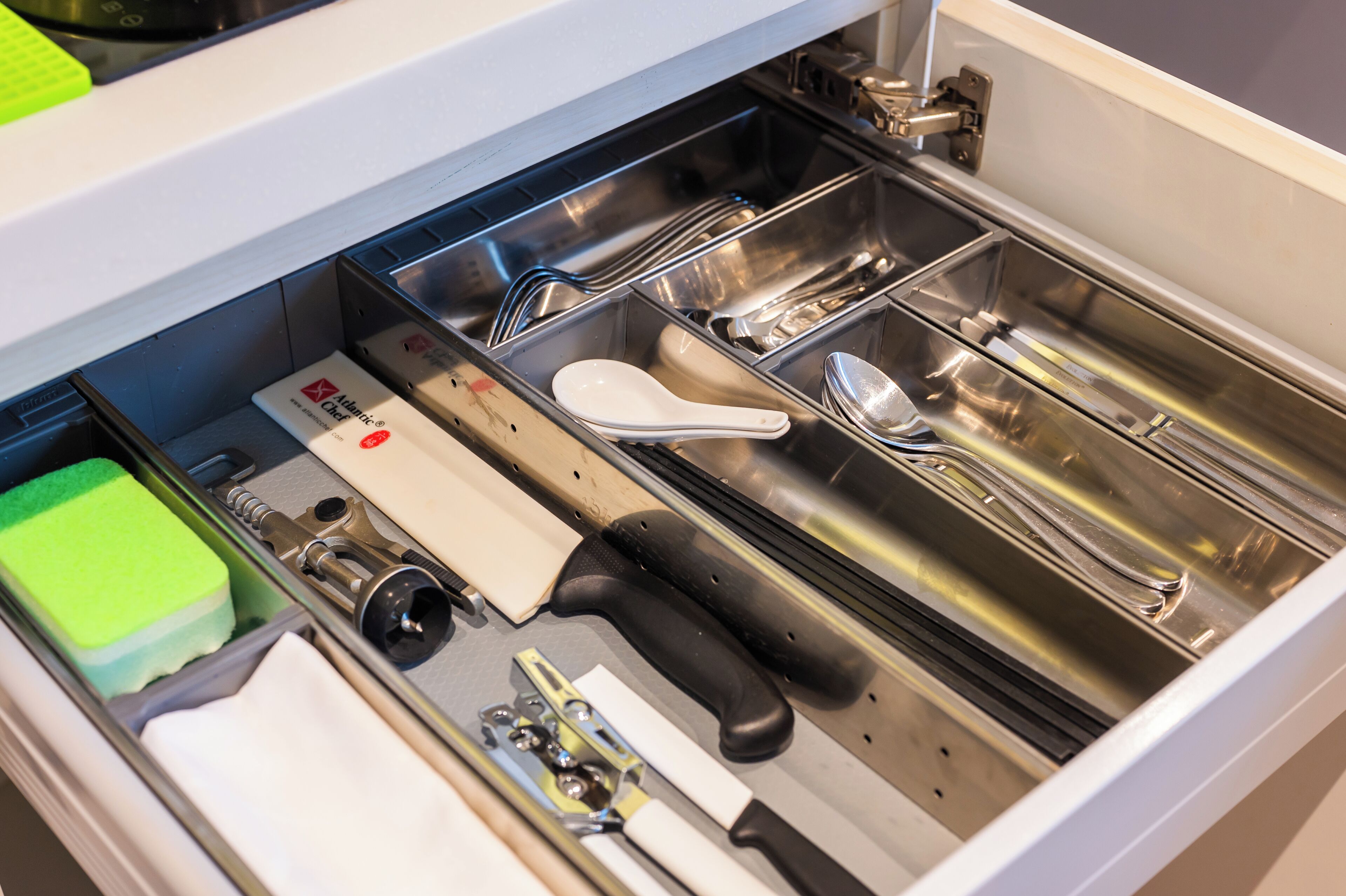 Un cajón de cocina con utensilios y una esponja verde.