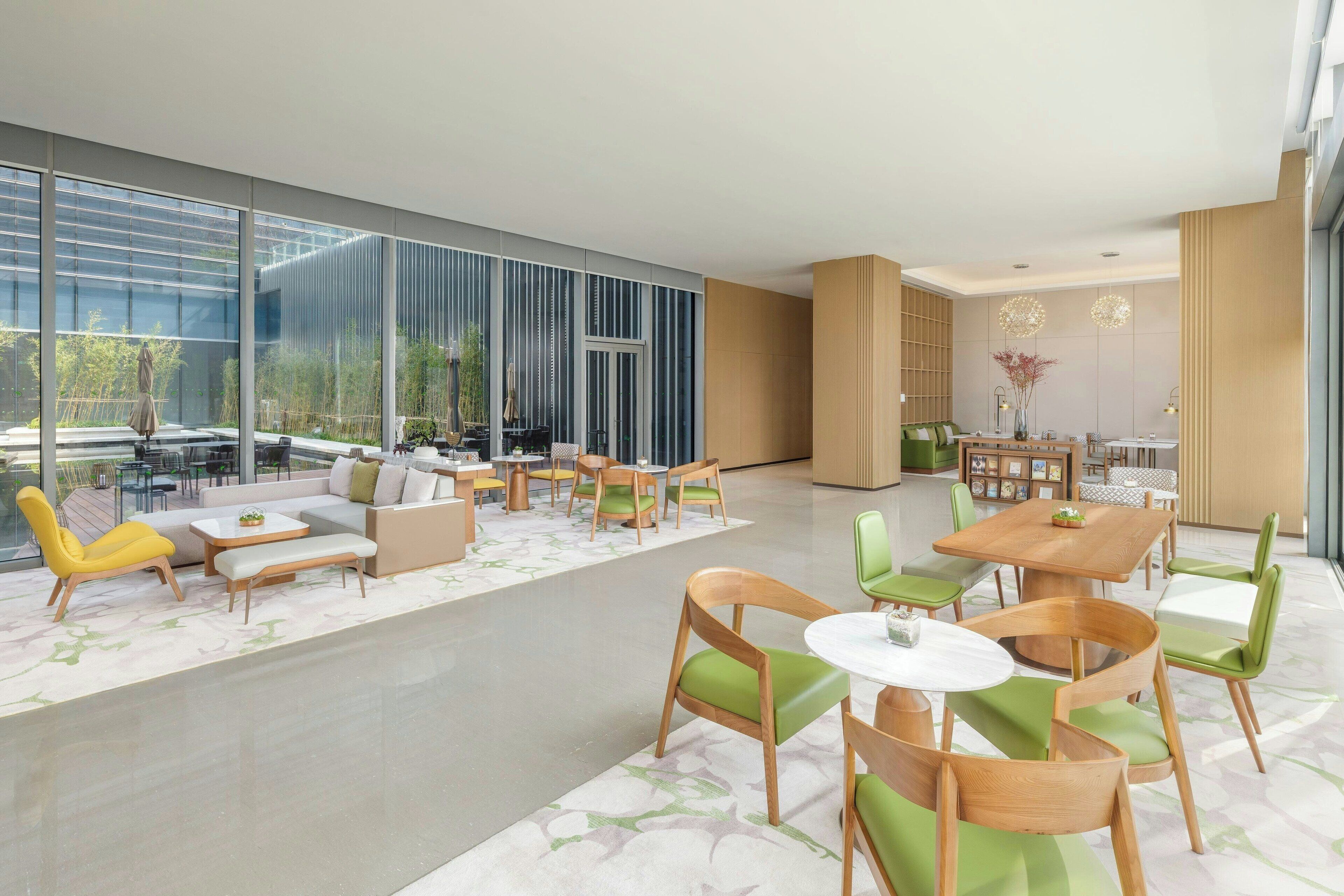 A spacious lobby with a modern design, featuring a seating area with sofas and chairs, a coffee table, and a dining area with a wooden table and chairs.