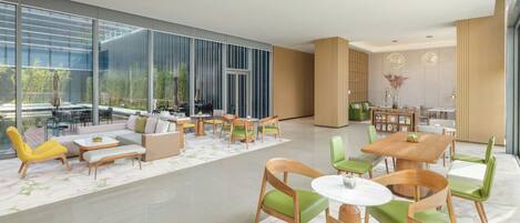 A spacious lobby with a modern design, featuring a seating area with sofas and chairs, a coffee table, and a dining area with a wooden table and chairs.