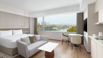 A modern hotel room with a bed, sofa, dining table, chairs, and a TV.