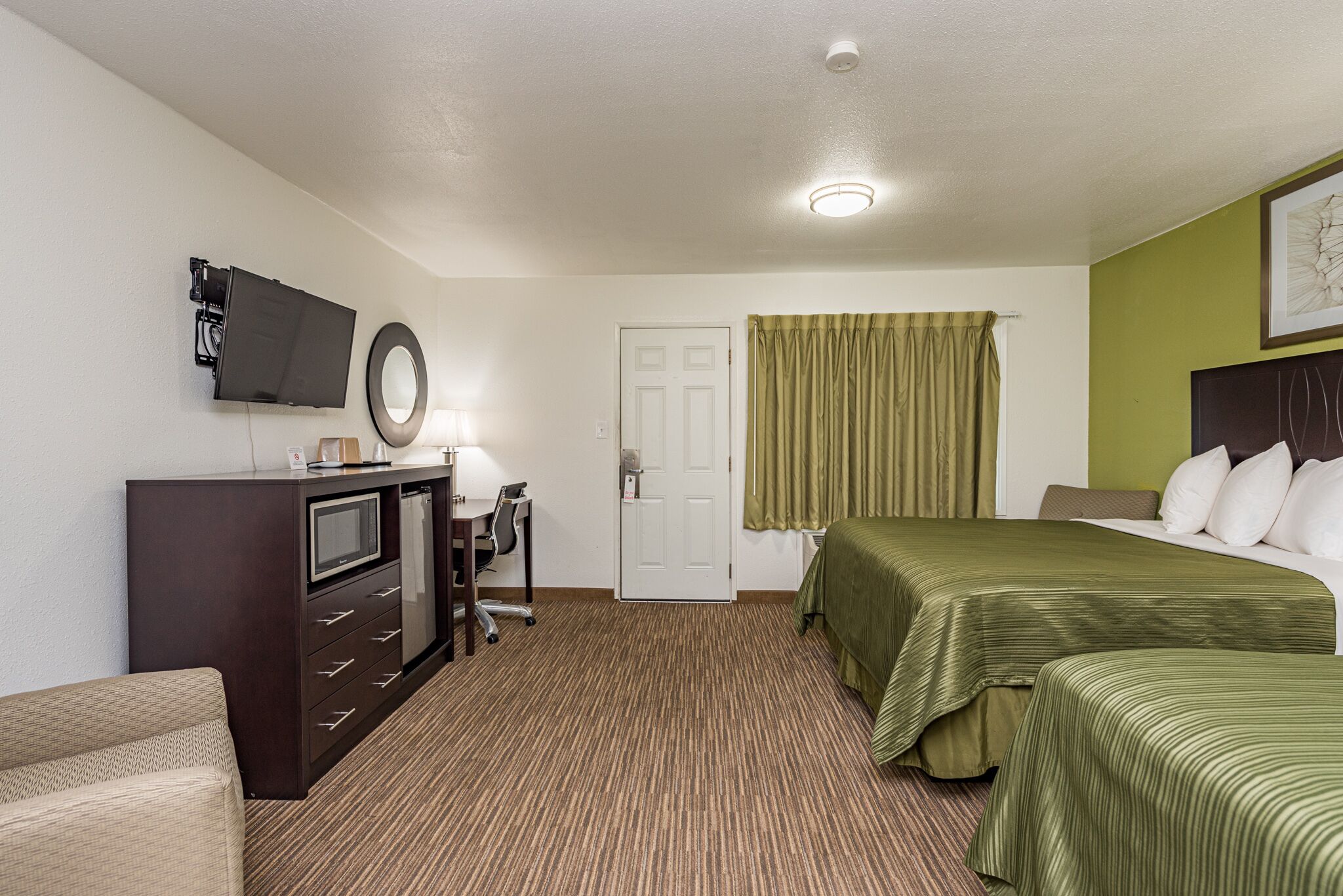 Una habitación de hotel con una cama, un escritorio con una silla, un televisor y una puerta.