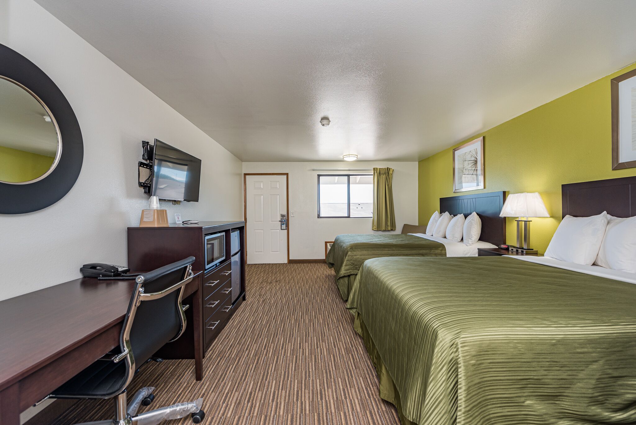 A hotel room with a desk, two beds, a TV, and a window with curtains.