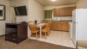 Cocina compacta con armarios de madera, microondas, refrigerador y comedor con mesa y sillas.
