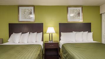 A hotel room with two beds, a nightstand with a lamp, and two framed pictures on the wall.