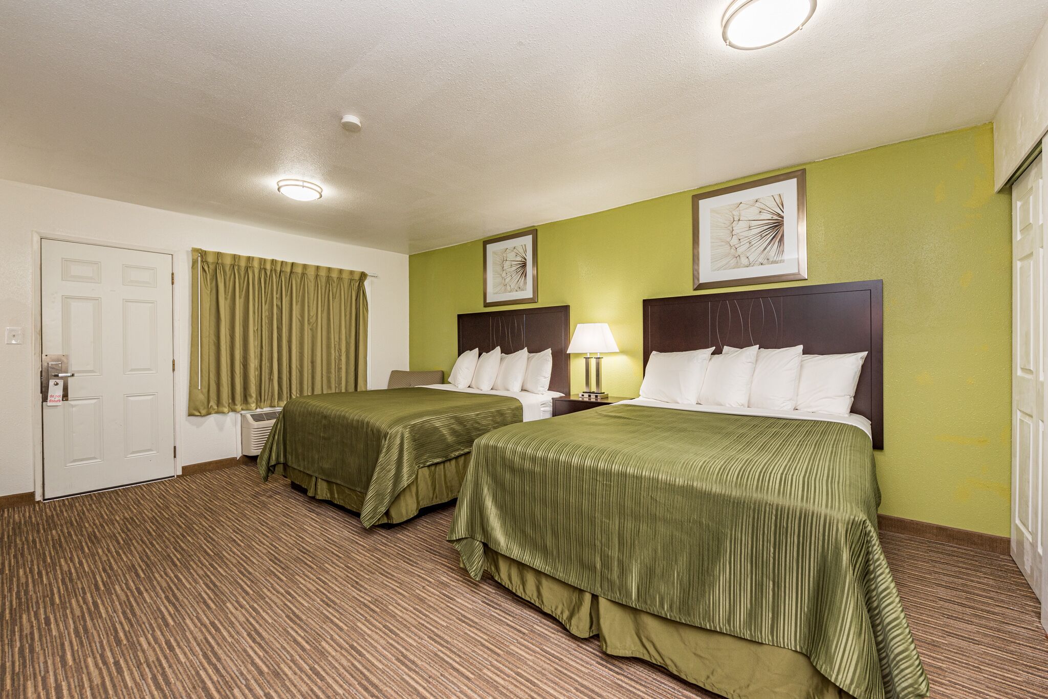 Een hotelkamer met twee bedden, groen beddengoed, een hoofdeinde met een lamp en kunst aan de muren.