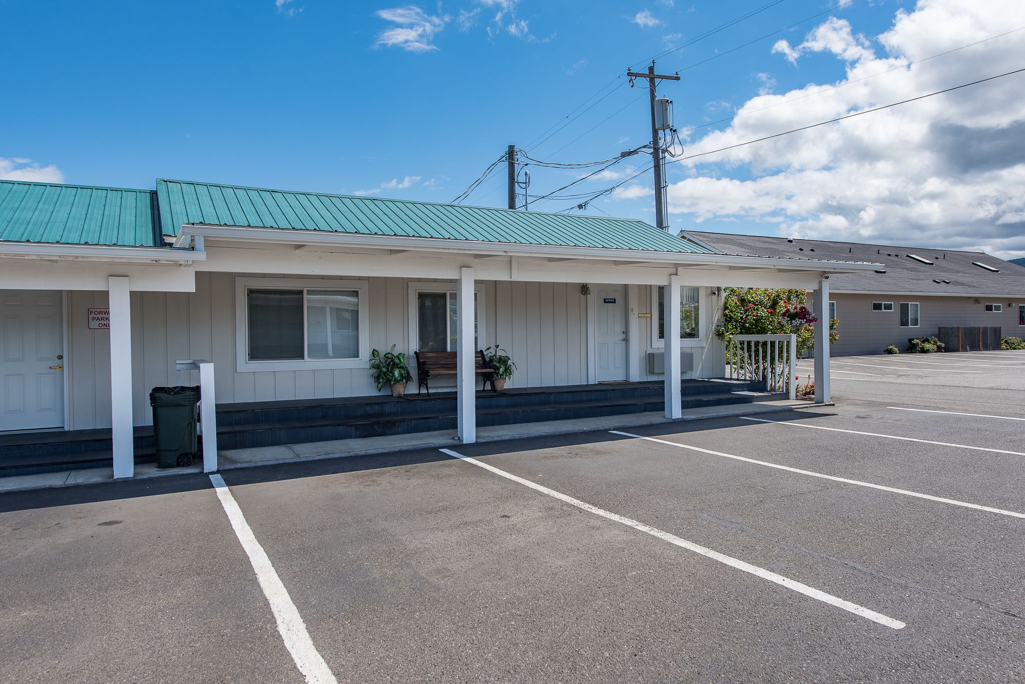 A motel with a green roof, white exterior, and a parking lot.