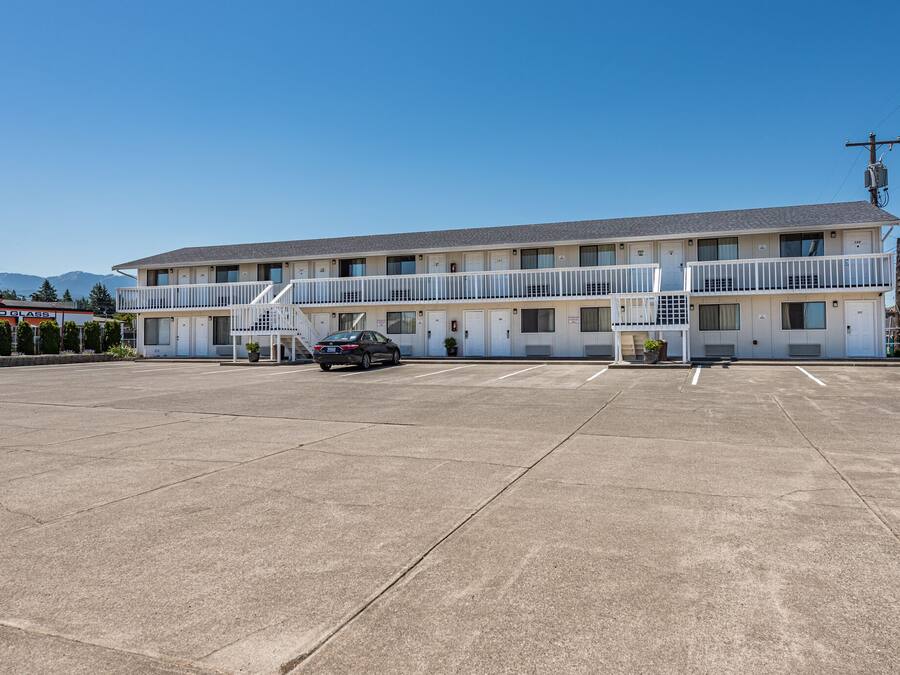 Un motel con una estructura de dos pisos, estacionamiento y montañas al fondo.