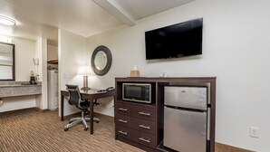 Habitación de hotel con kitchenette, televisor de pantalla plana, escritorio con silla, microondas, refrigerador, espejo y piso alfombrado.
