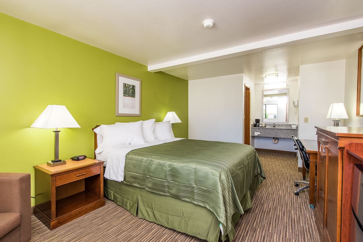 Habitación de hotel con cama, mesitas de noche, escritorio, silla, espejo y baño con lavabo y espejo.