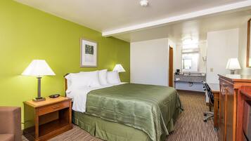 Een hotelkamer met een bed, nachtkastjes, een bureau, een stoel, een spiegel en een badkamer met een wastafel en spiegel.
