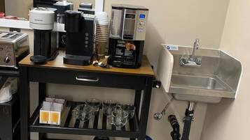 A kitchenette with a coffee machine, a sink, and a storage shelf with cups and a kettle.