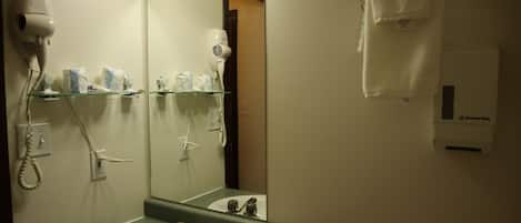 Un bagno con lavandino, specchio, asciugacapelli e portasciugamani.