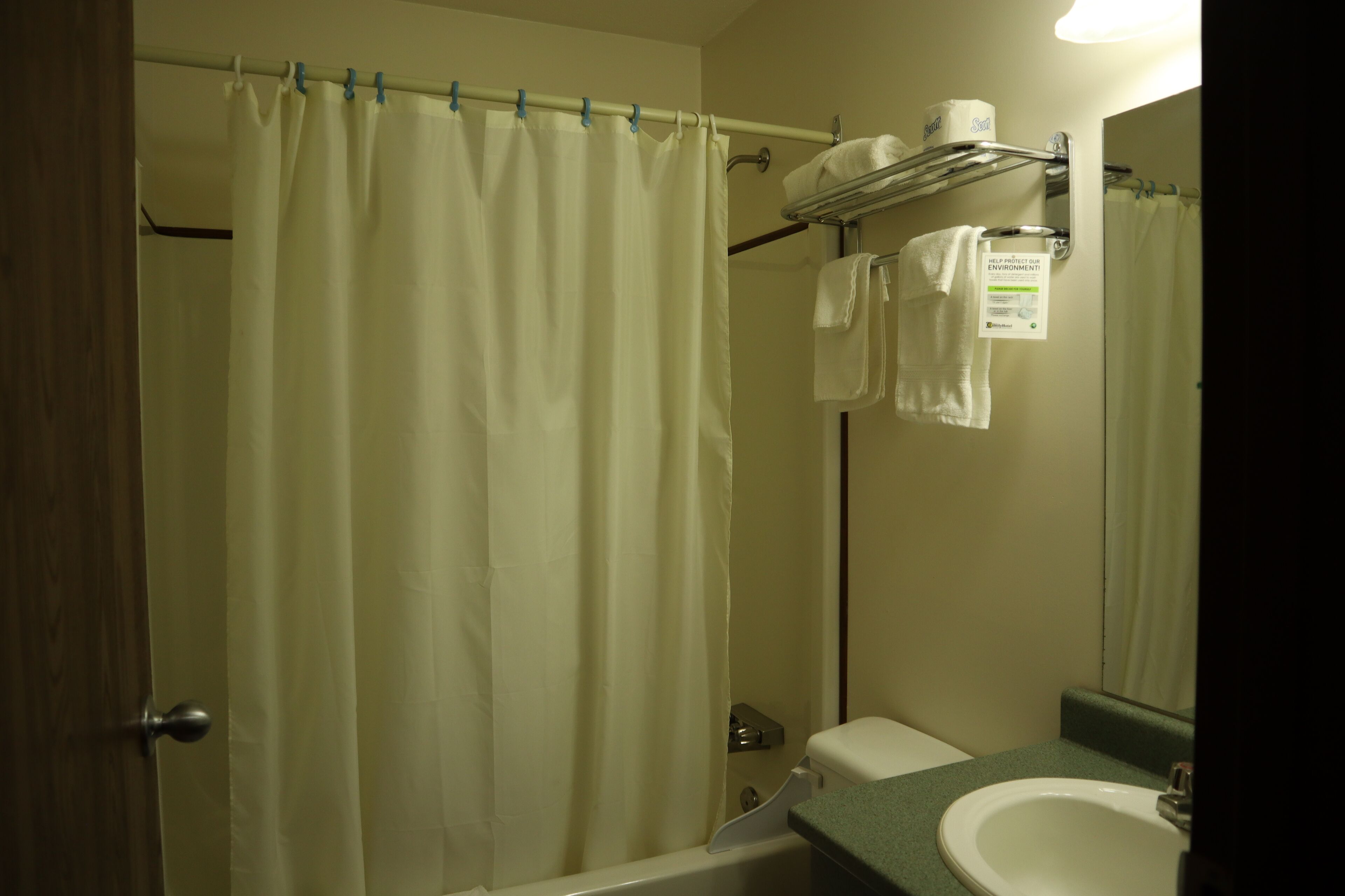 Ein Badezimmer mit Duschvorhang, Handtuchhalter mit Handtüchern, Toilette und Waschbecken mit Spiegel.