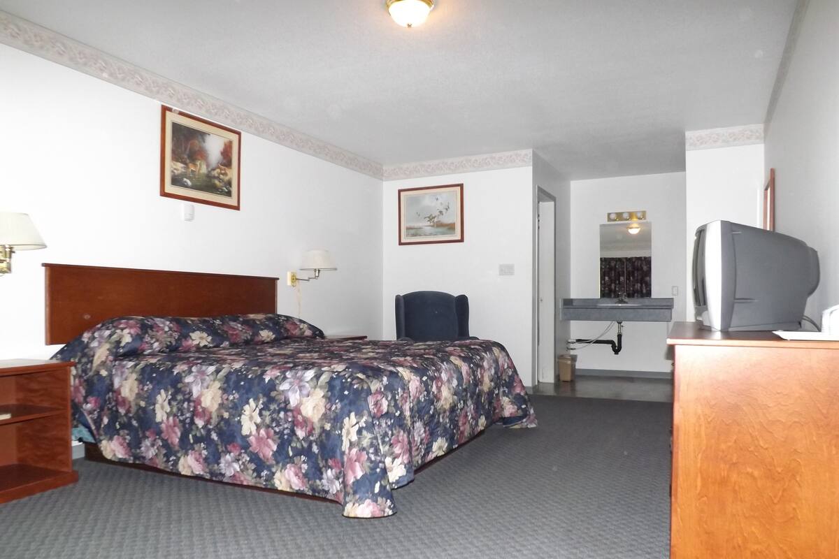 A hotel room with a bed, a desk with a television, a chair, and a bathroom visible in the background.