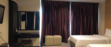 A hotel room with a bed, a desk, a chair, a television, and a large window with curtains.
