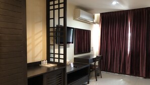 Een moderne woonkamer met een donker houten roomdivider, een flatscreen televisie aan de muur, een zwart tv-meubel en een groot raam met donkere gordijnen.