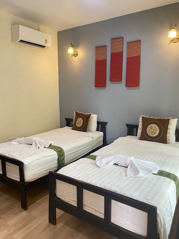 Two single beds with headboards, a wall-mounted air conditioner, and two wall-mounted light fixtures.