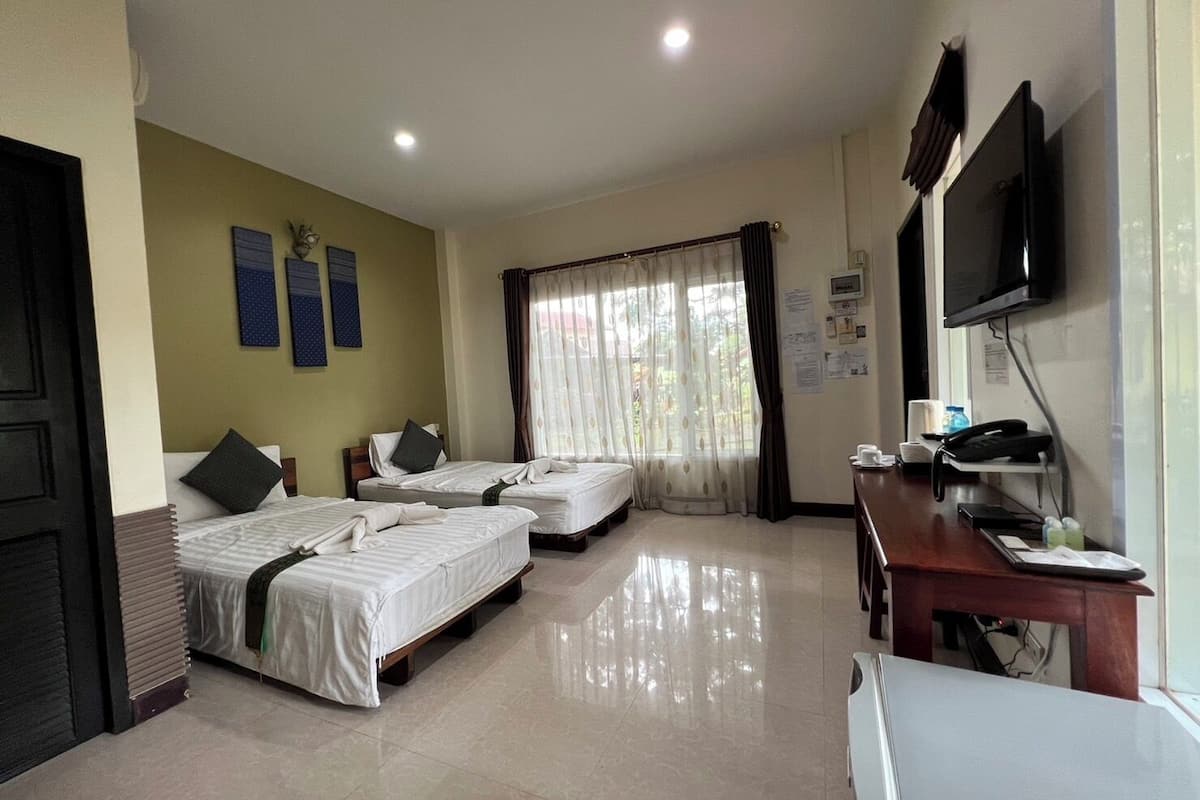A hotel room with three beds, a desk with a computer, a TV, and a window with curtains.