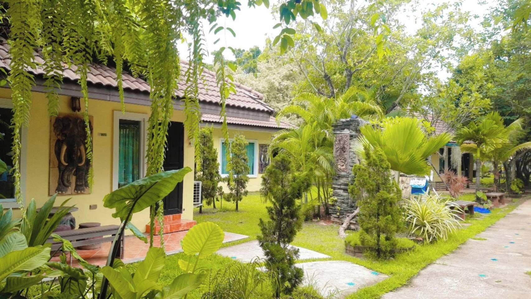 A yellow building with a tiled roof, surrounded by lush greenery and a stone pillar.