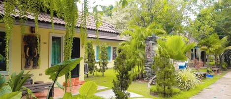 A yellow building with a tiled roof, surrounded by lush greenery and a stone pillar.