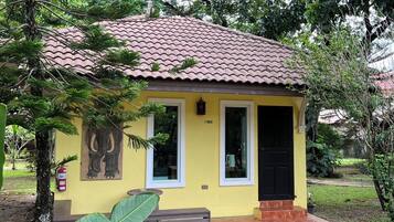 Um pequeno edifício amarelo com telhado de azulejos, porta preta e um banco na frente.
