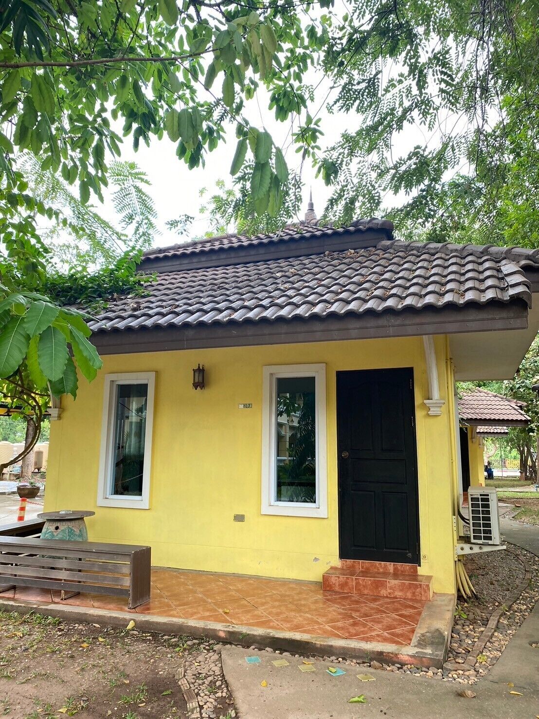 A small yellow building with a tiled roof, a black door, and a window.