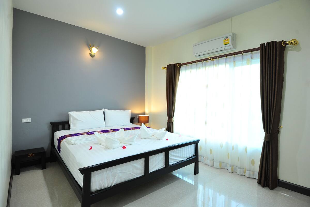A neatly made bed with white linens, a bedside table with a lamp, and a window with curtains.