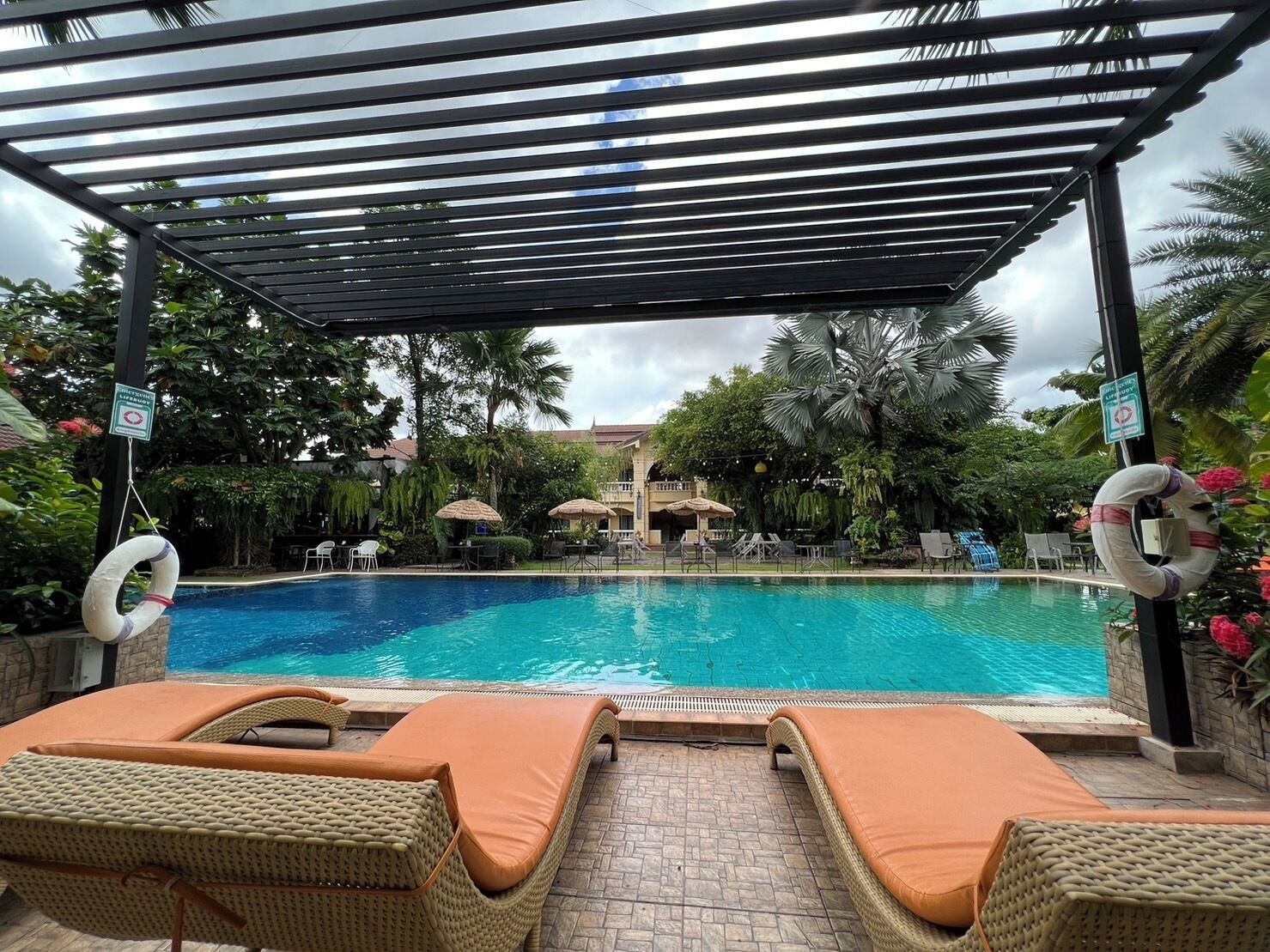 A pool area with lounge chairs, a pergola, and palm trees.