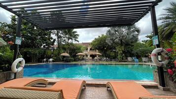 A pool area with lounge chairs, a pergola, and palm trees.