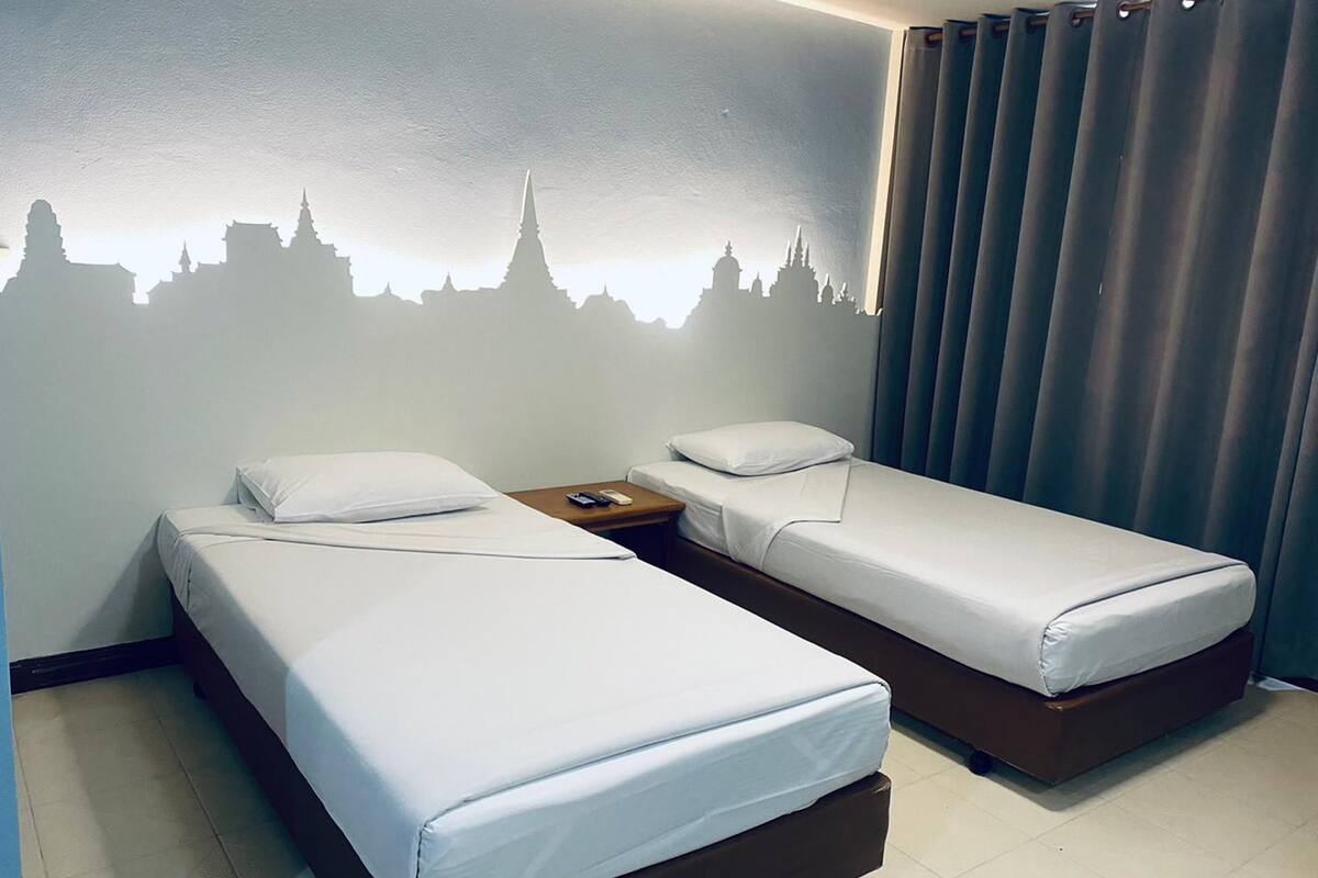 A hotel room with two single beds, a nightstand, and a wall mural of a city skyline.