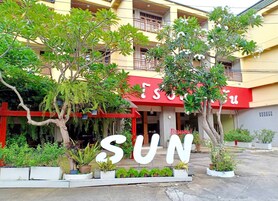 A hotel entrance with a large 'SUN' sign, surrounded by potted plants and trees.