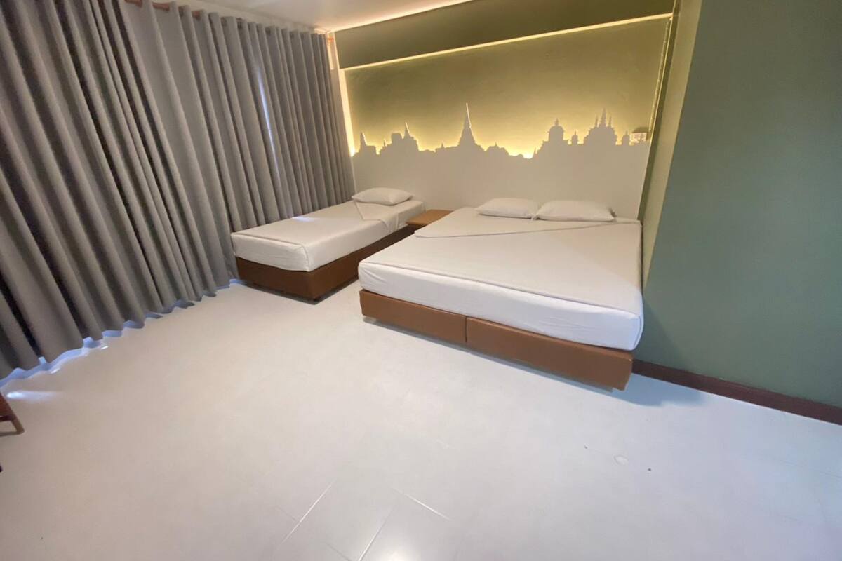 A hotel room with two beds, a city skyline mural on the wall, and a large window with curtains.