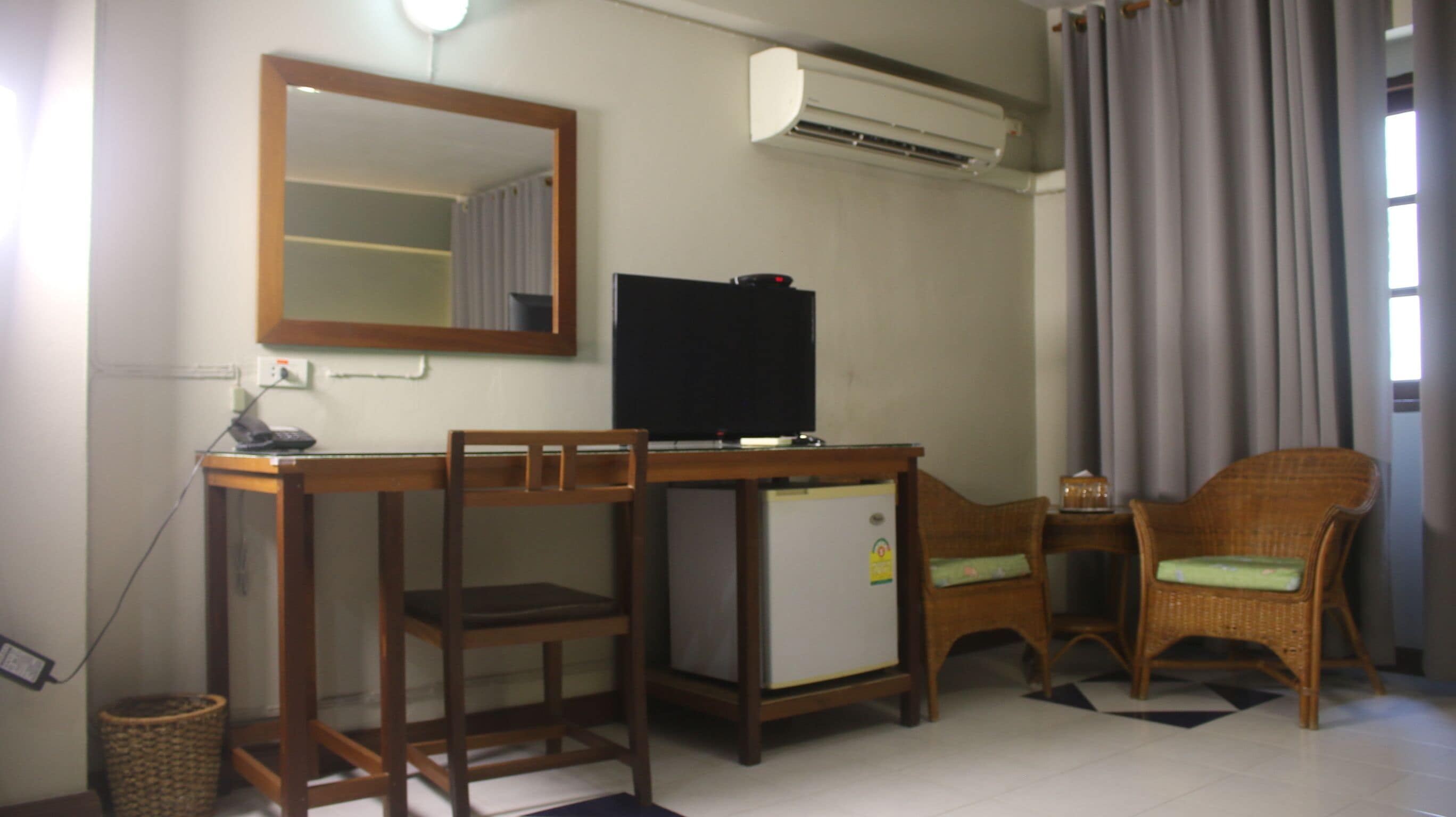 A room with a desk, two chairs, a television, and an air conditioner.