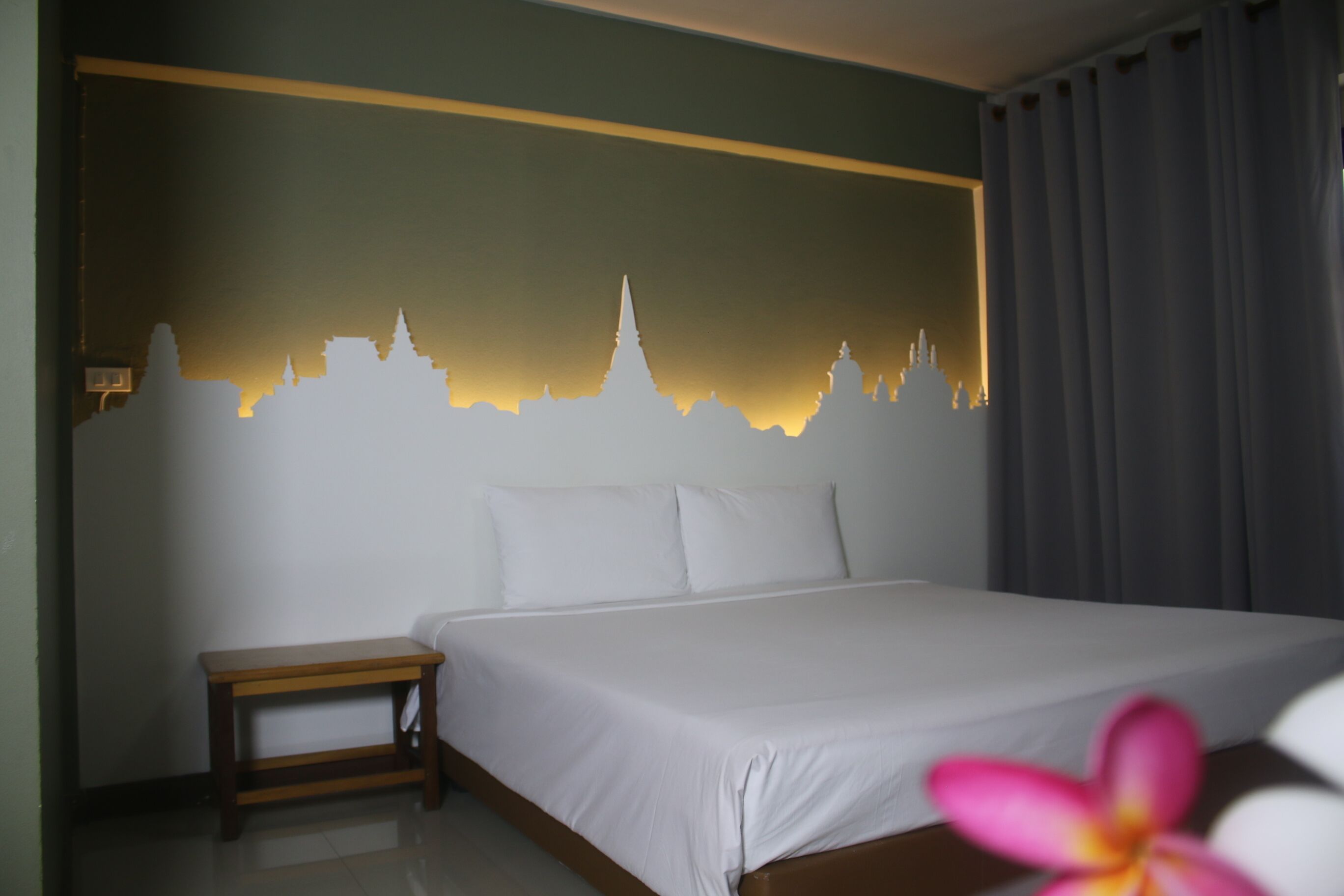 Habitación de hotel con cama, mesita de noche pequeña y un mural en la pared con un horizonte urbano.