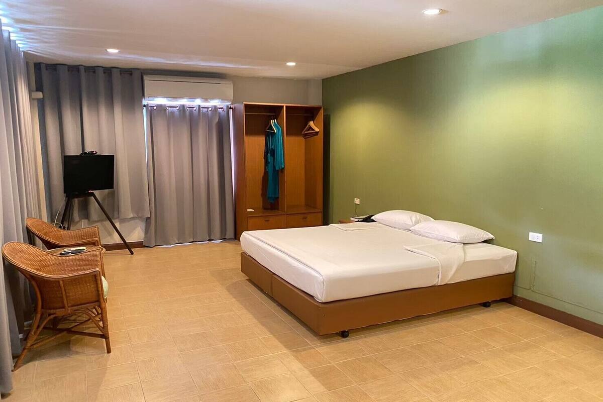 A hotel room with a bed, a desk, a chair, a wardrobe, and a television.