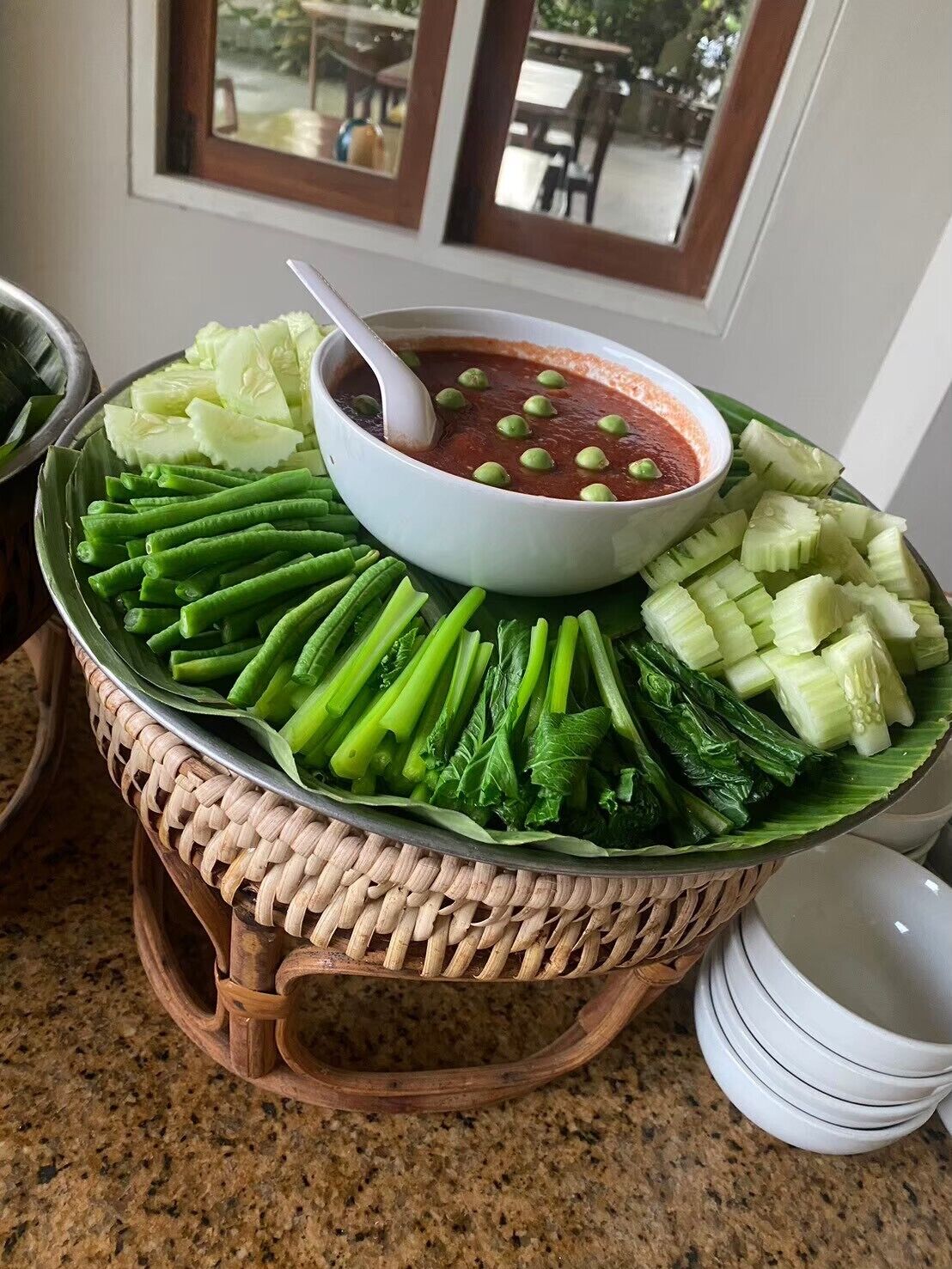Une présentation de plats comprenant un bol de sauce et divers légumes disposés sur un plateau en osier.