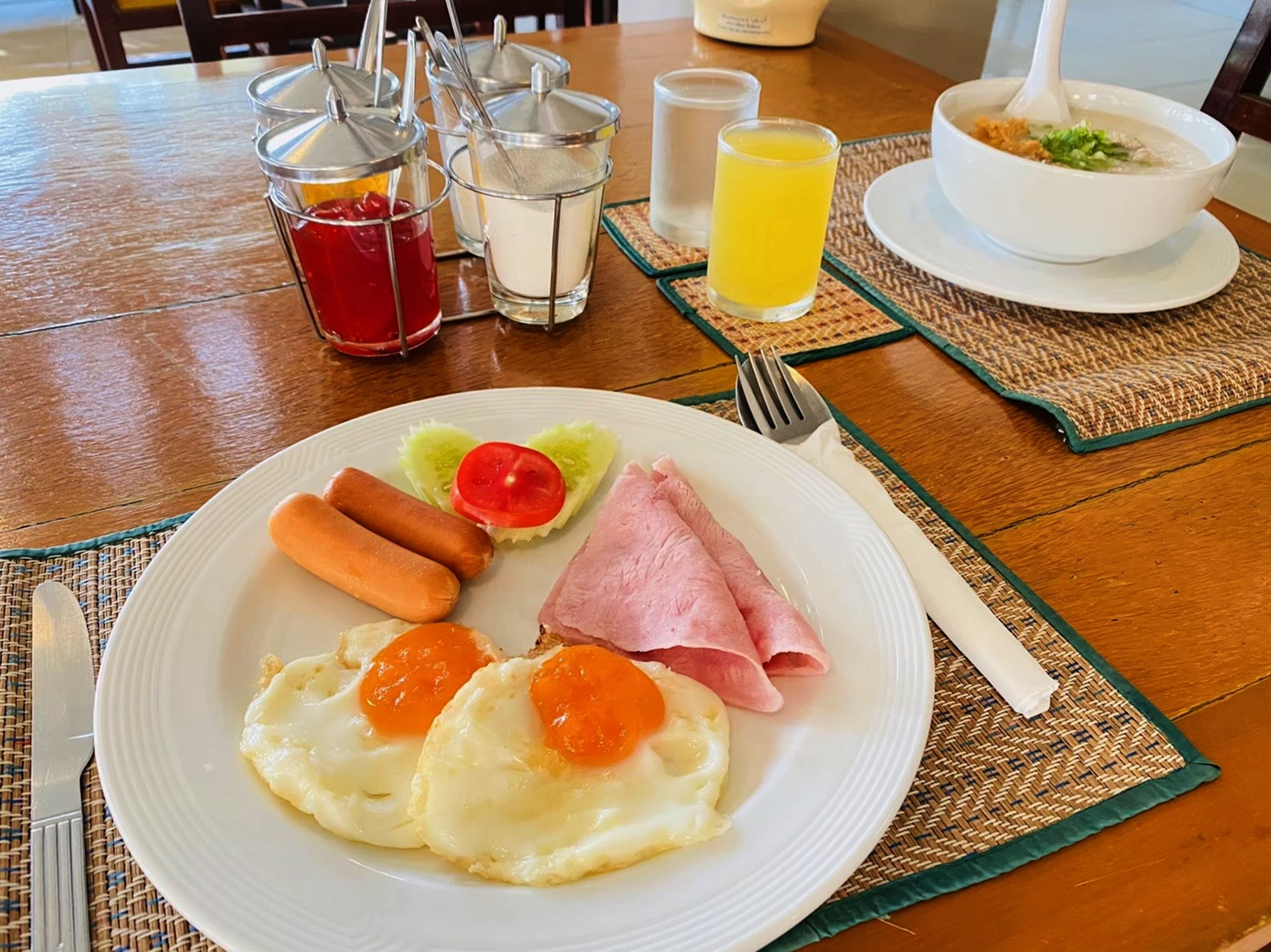 A breakfast plate with eggs, sausages, ham, and a slice of tomato.