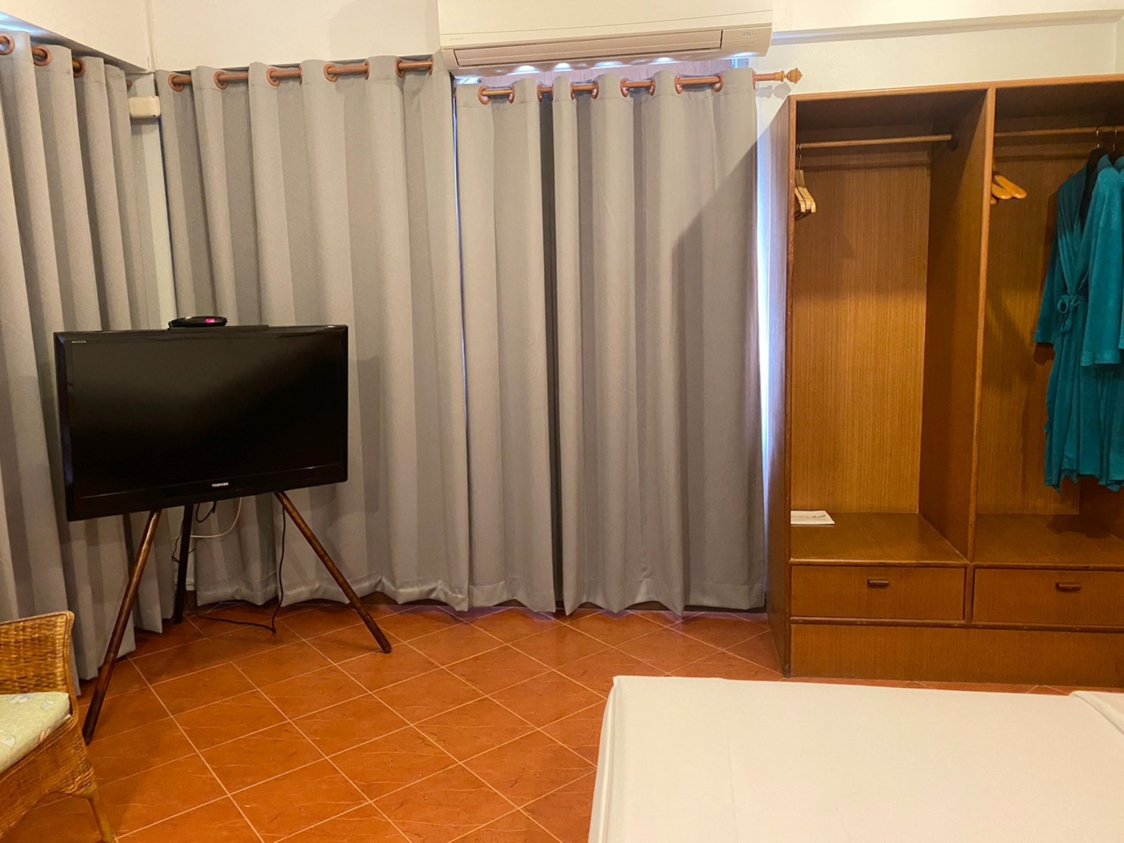 Habitación de hotel con televisión sobre un mueble, cortinas grises, un armario de madera y una cama.