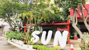 Um grande letreiro ao ar livre com a palavra "SUN" em letras brancas, cercado por vegetação e árvores.