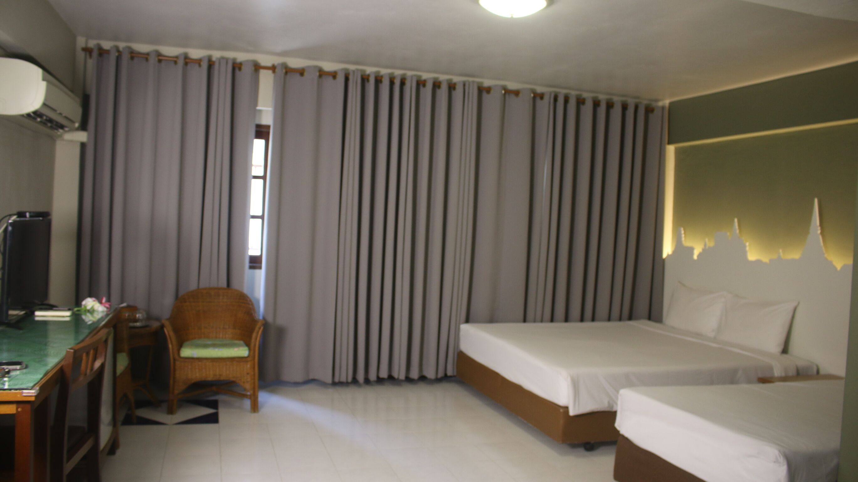 Habitación de hotel con dos camas, un escritorio con silla, un equipo de aire acondicionado y una ventana con cortinas.