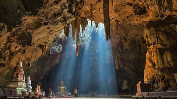 A cave temple with a large Buddha statue, stone carvings, and a row of benches.