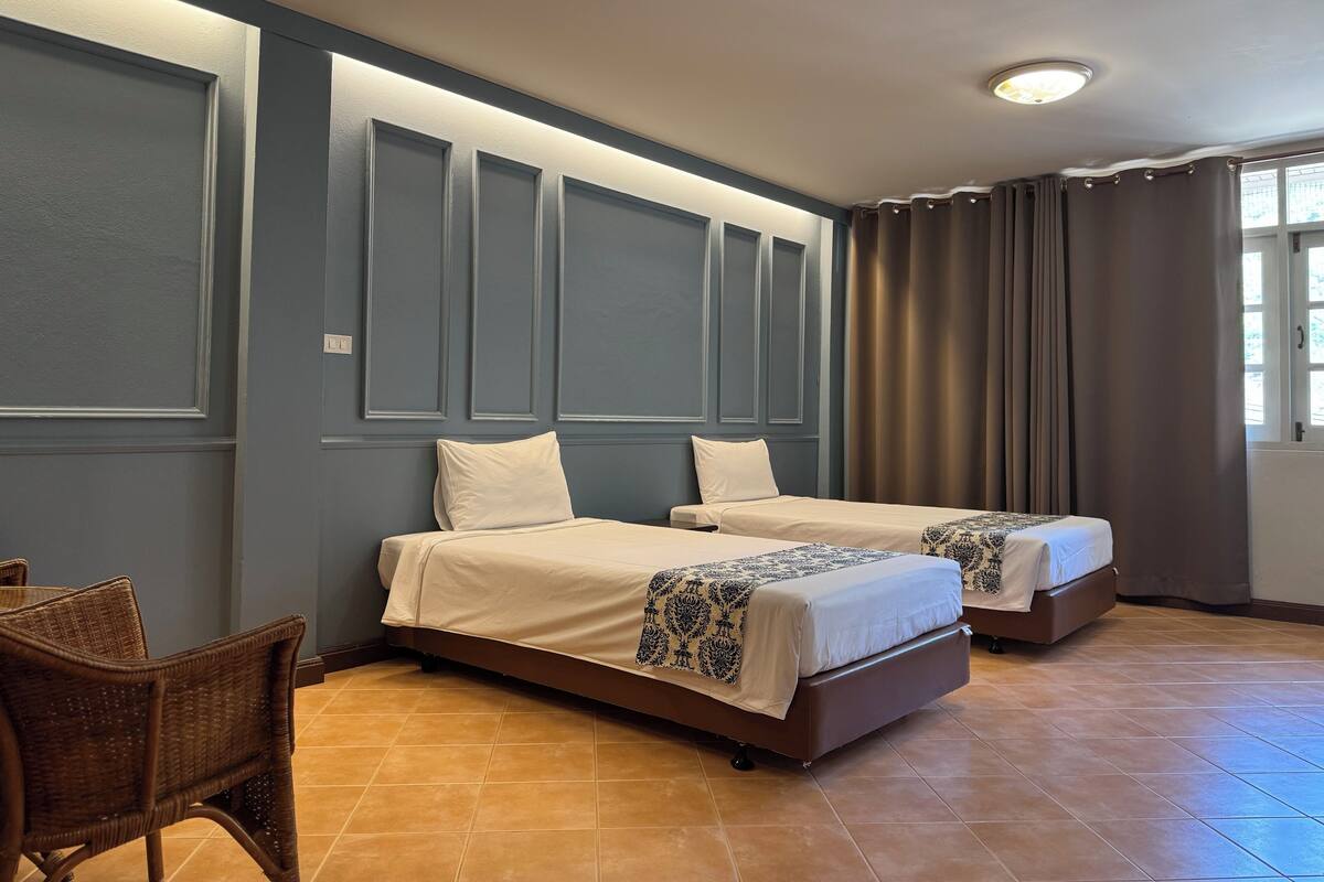 A hotel room with two beds, a chair, and a window with curtains.