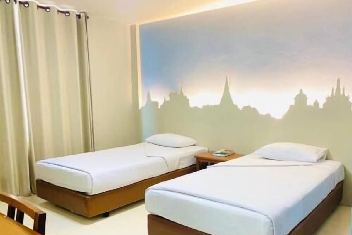 A hotel room with two single beds, a wooden headboard, a nightstand, and a cityscape mural on the wall.